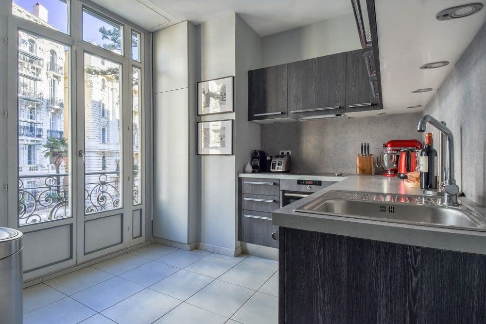 Kitchen with dark units, stainless steel sink and French windows to a balcony, 2-bedroom apartment in the Carré d’Or, Nice