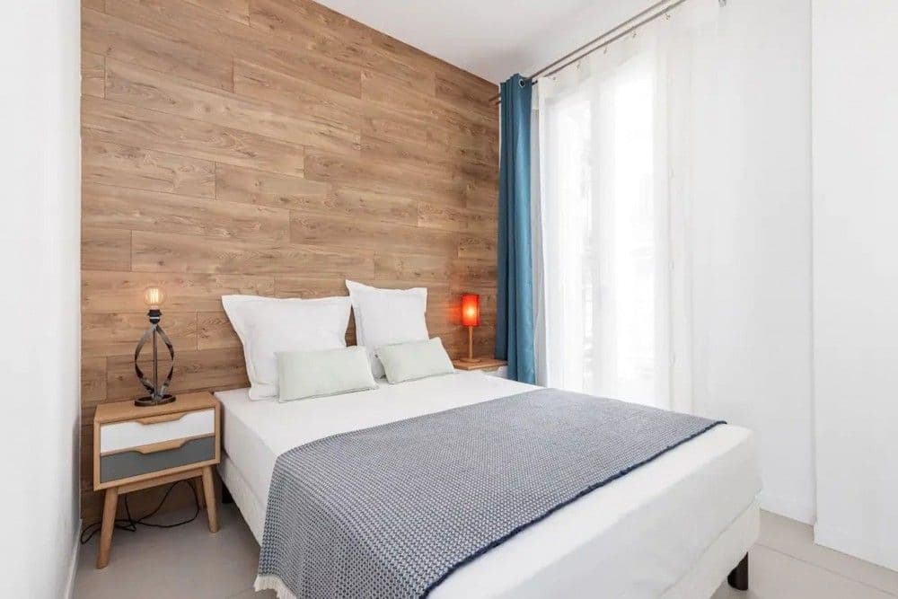 Bedroom with wood-panelled wall and window, 2-bedroom apartment in the Promenade des Anglais, Nice