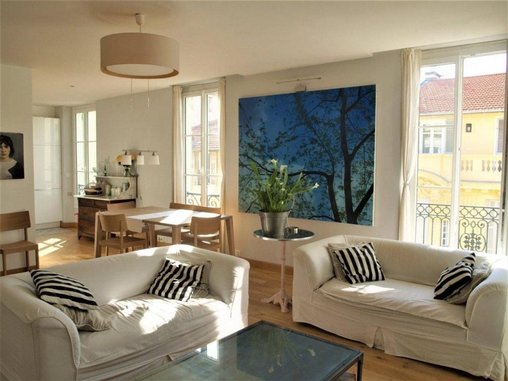 Living and dining room with oak floor and tall windows, 2-bedroom apartment in the Carré d’Or, Nice