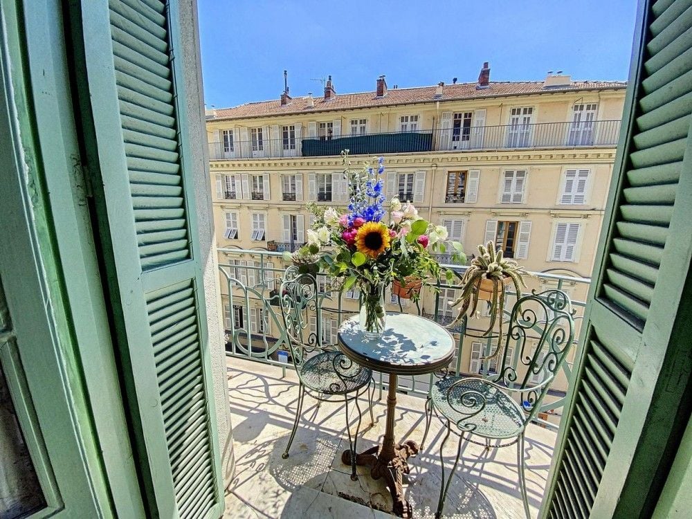 Balcony with bistro table, flowers and a view of Belle Époque façades, 2-bedroom apartment in the Port, Nice