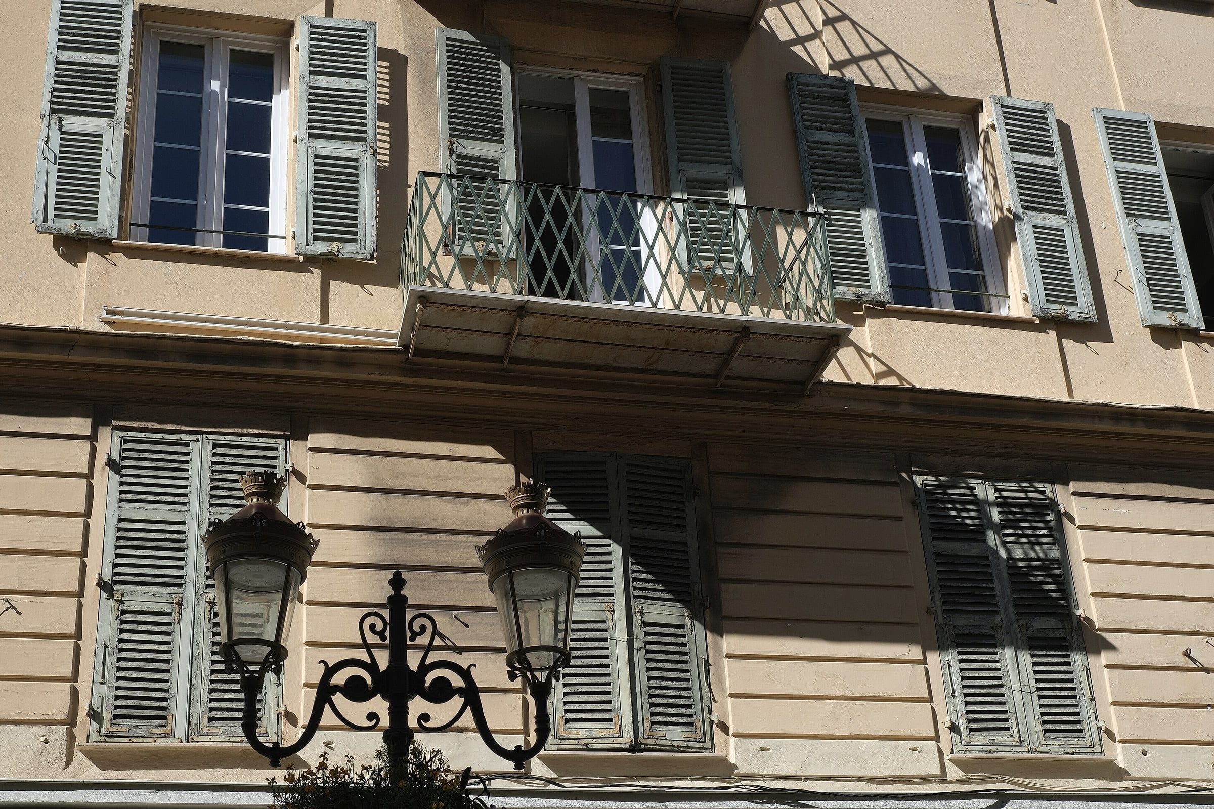 A wrought-iron street lamp in front of a shuttered façade on Rue Paradis