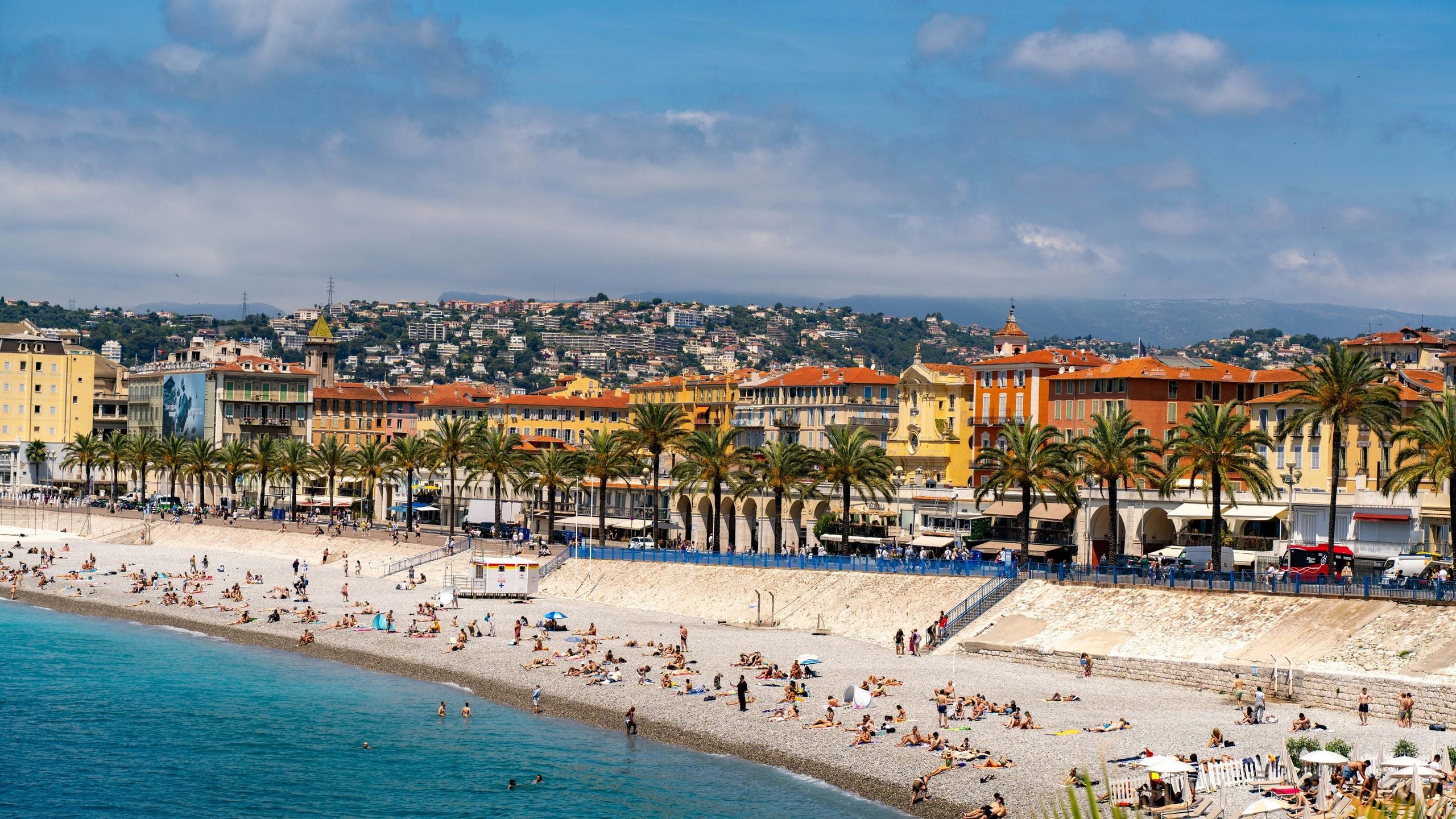 The pebble beach below the Quai des États-Unis in Nice, ochre façades and palms along the seafront