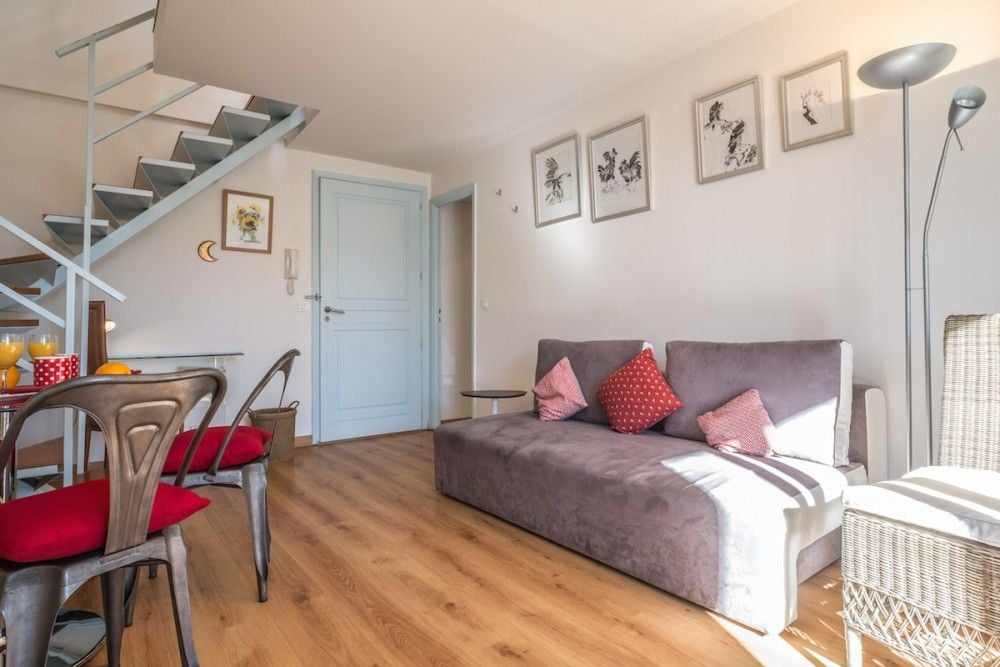 Living room with sofa, dining table and spiral staircase, 1-bedroom apartment in the Carré d’Or, Nice