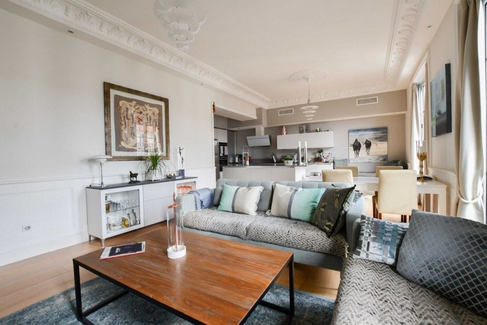 Living area with wooden coffee table and the open kitchen behind, 3-bedroom apartment in the Carré d’Or, Nice