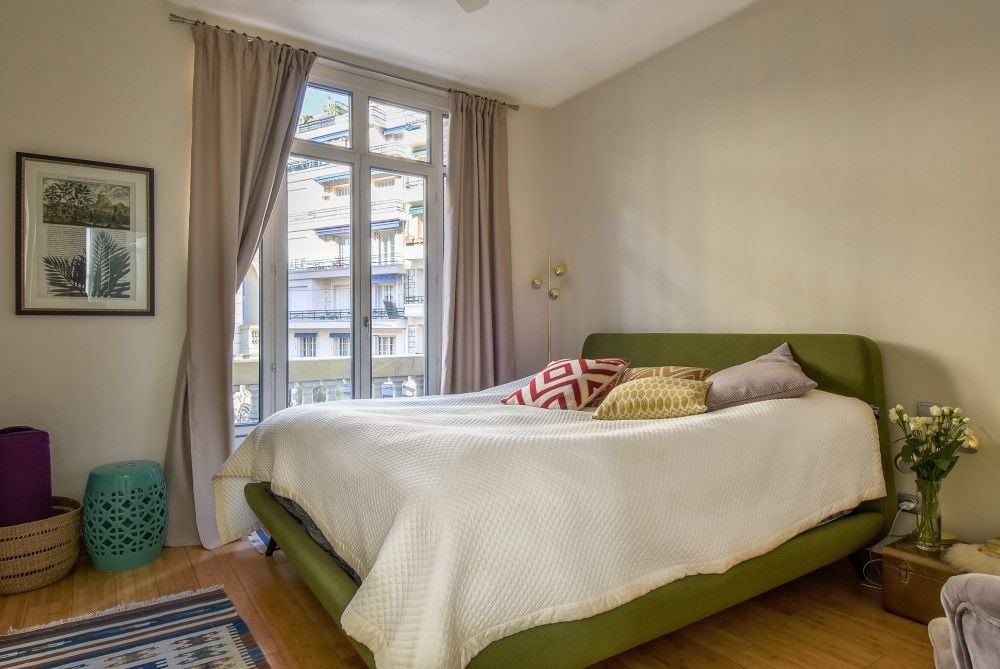 Bedroom with green upholstered bed and tall window, 2-bedroom apartment in the Carré d’Or, Nice