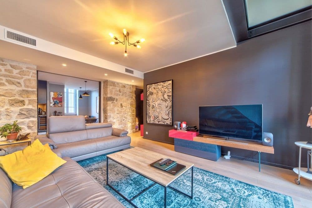 Living room with exposed stone wall, sofa and blue rug, 2-bedroom apartment in the Port, Nice