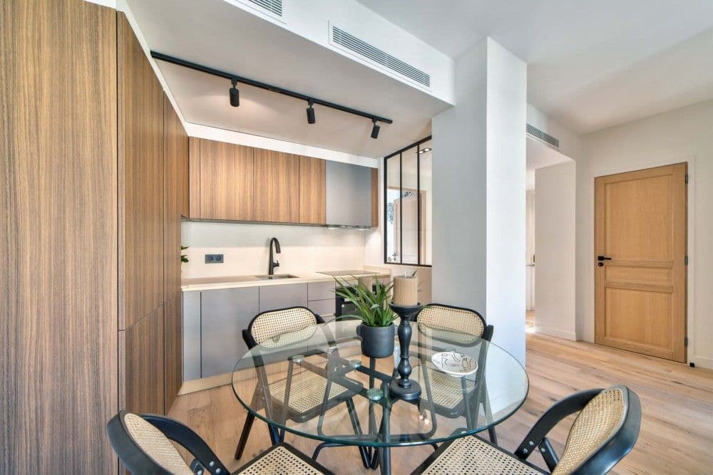 Dining area with glass table and kitchen behind a glass partition, 2-bedroom apartment in the Carré d’Or, Nice
