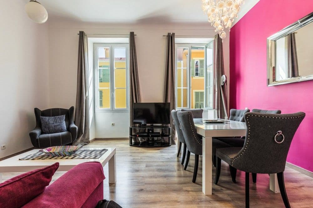 Living and dining room with pink feature wall and chandelier, 2-bedroom apartment in the Port, Nice