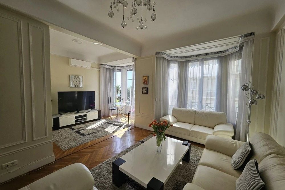Living room with bay window, white leather sofas and herringbone parquet, 3-bedroom apartment in the Promenade des Anglais, Nice