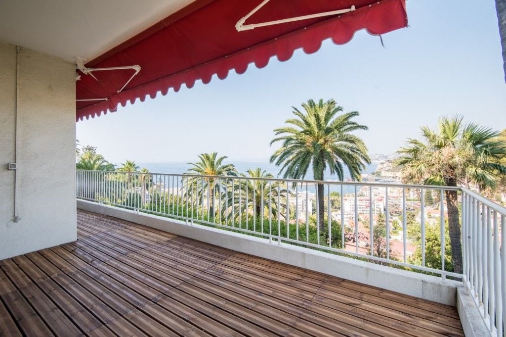 Terrace with red awning, wooden deck and sea view through palms, 2-bedroom apartment in Mont Boron, Nice