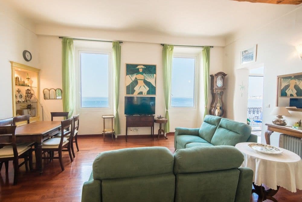 Living room with green sofas, dining table and sea-view windows, 3-bedroom apartment in the Promenade des Anglais, Nice
