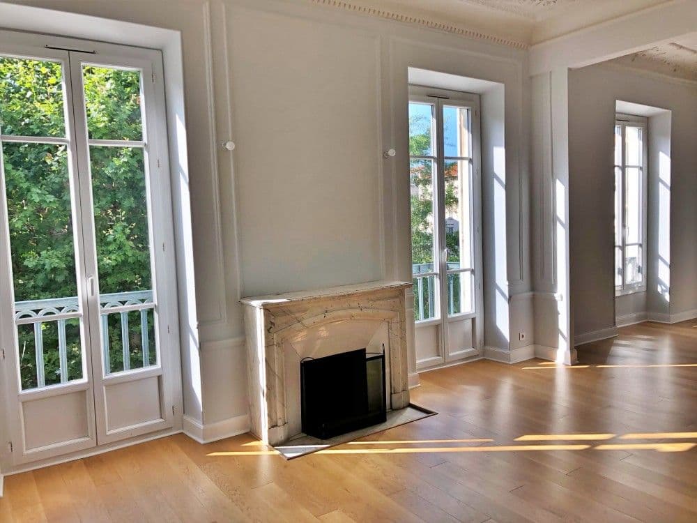 Empty living room with marble fireplace, oak floor and tall French windows onto balconies, 3-bedroom apartment in central Nice