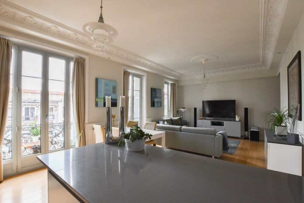 Open-plan living room with moulded ceilings, tall windows and a kitchen island, 3-bedroom apartment in the Carré d’Or, Nice