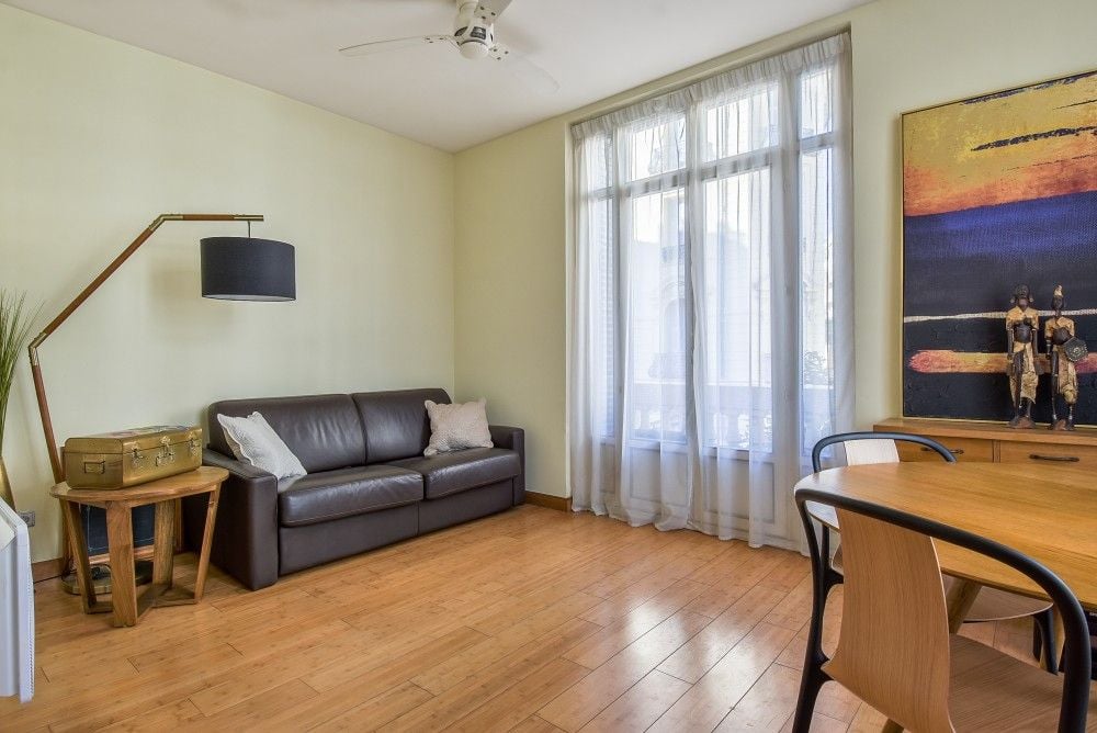 Living room with leather sofa, tall windows and wooden floor, 2-bedroom apartment in the Carré d’Or, Nice