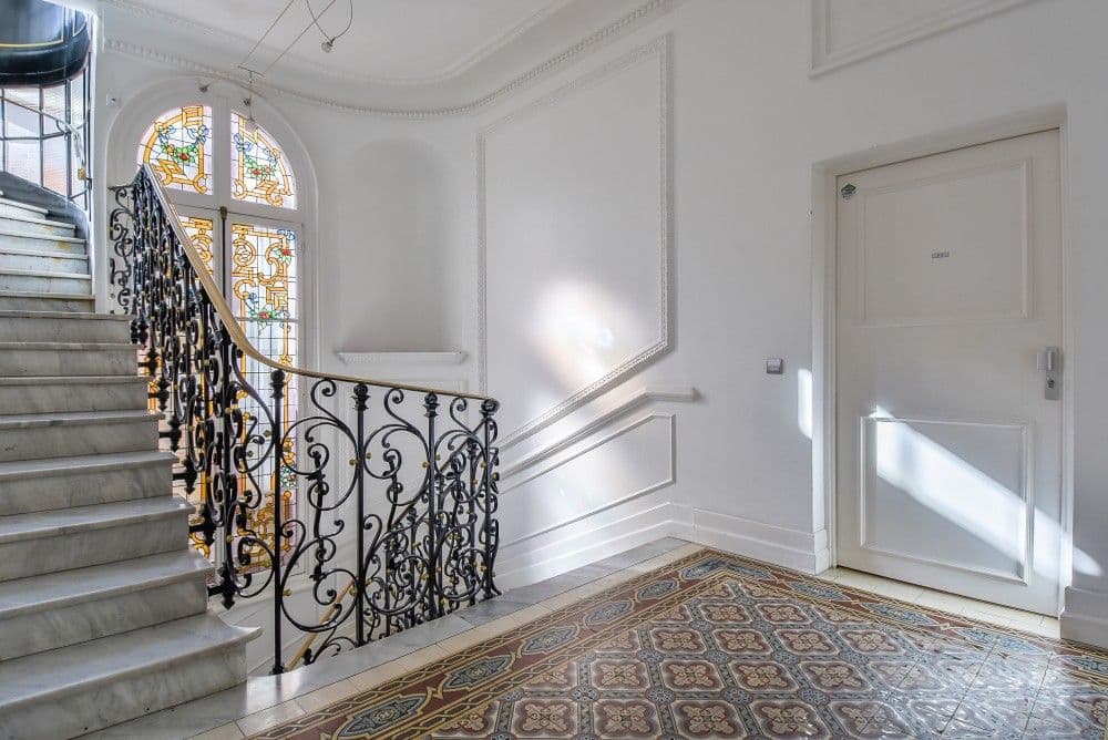 Belle Époque stairwell with wrought-iron banister and arched stained-glass window, 2-bedroom apartment in the Carré d’Or, Nice