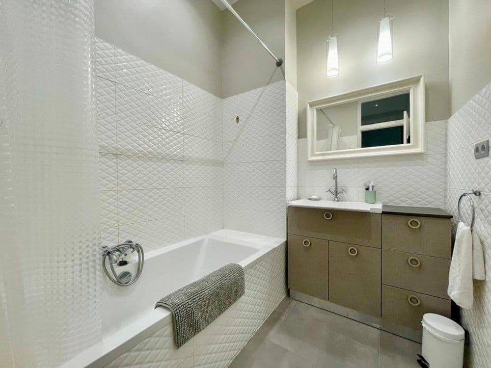 Bathroom with textured white tiles, bathtub and vanity unit, 2-bedroom apartment in Nice