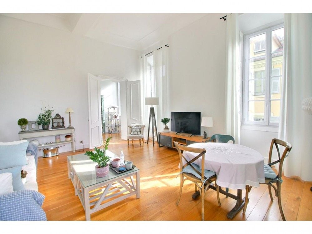 Living room with oak floor, tall windows and round dining table, 2-bedroom apartment in the Old Town, Nice